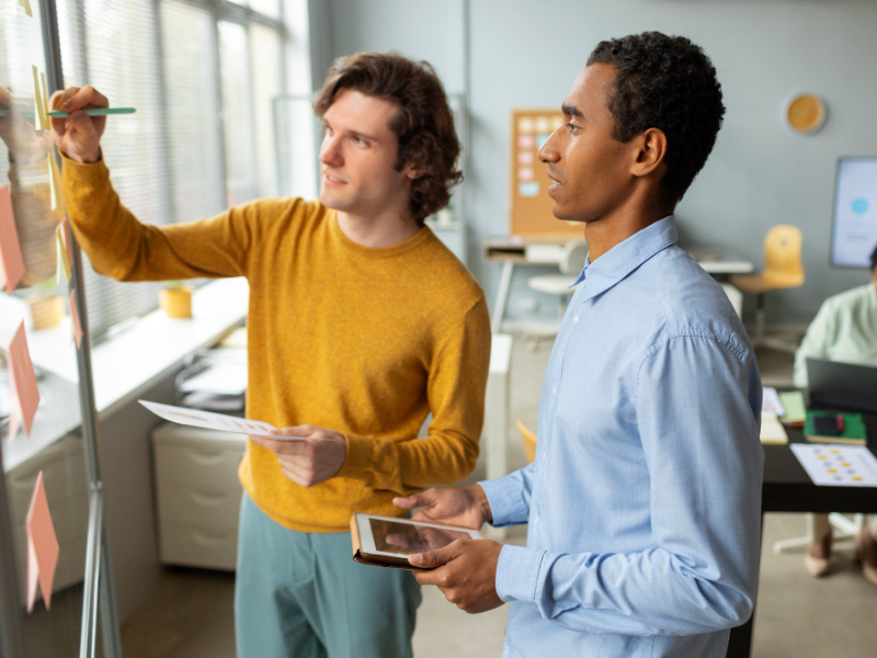 Team members review plans on a glass board, reflecting skilled-labour strategy and knowledge transfer in print operations.